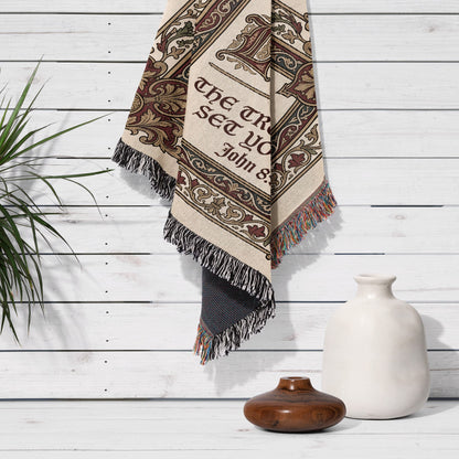 Woven tapestry with "The truth will set you free" text, fringed edges, hanging on wall.