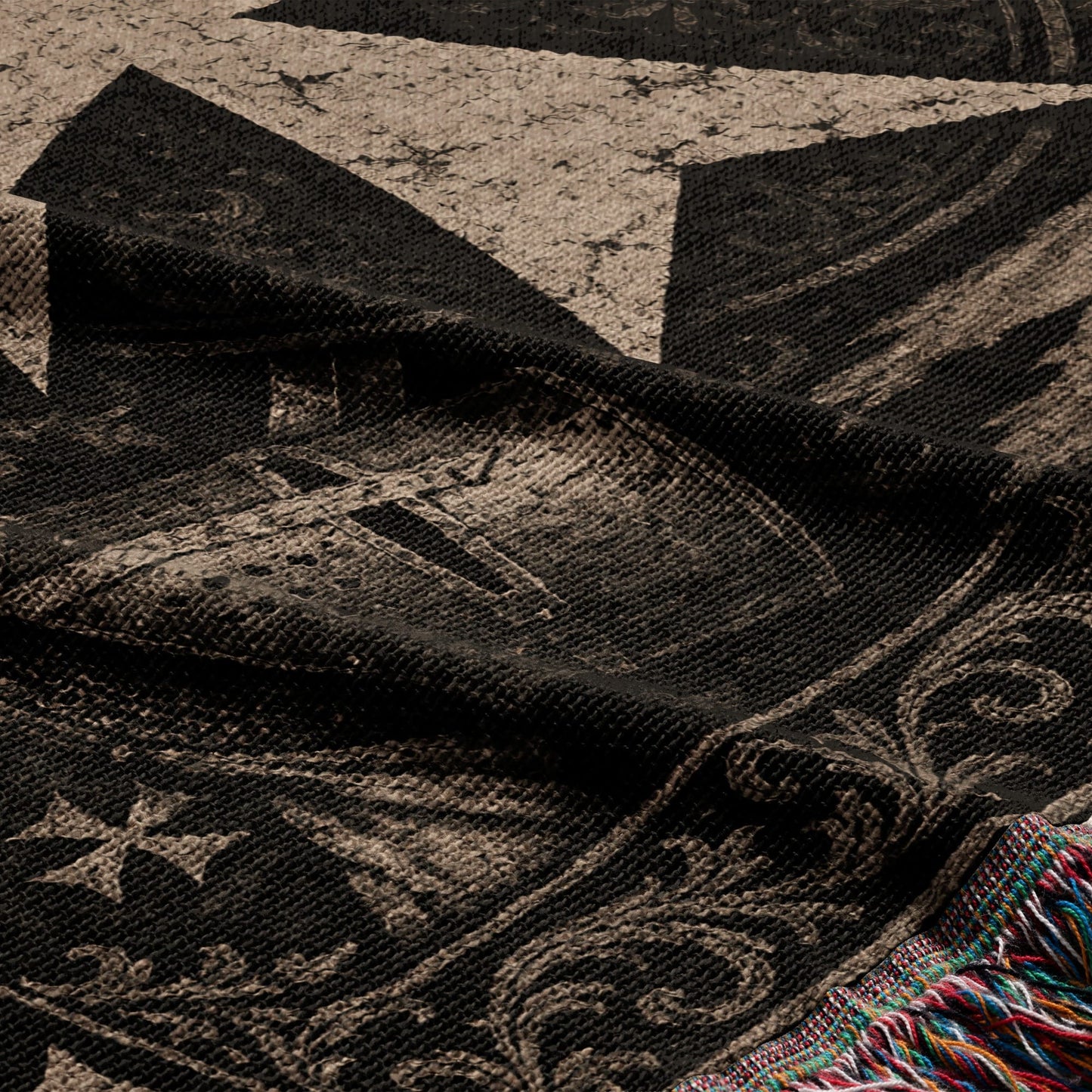 Dark woven throw blanket with an intricate vintage pattern and tasseled edge.