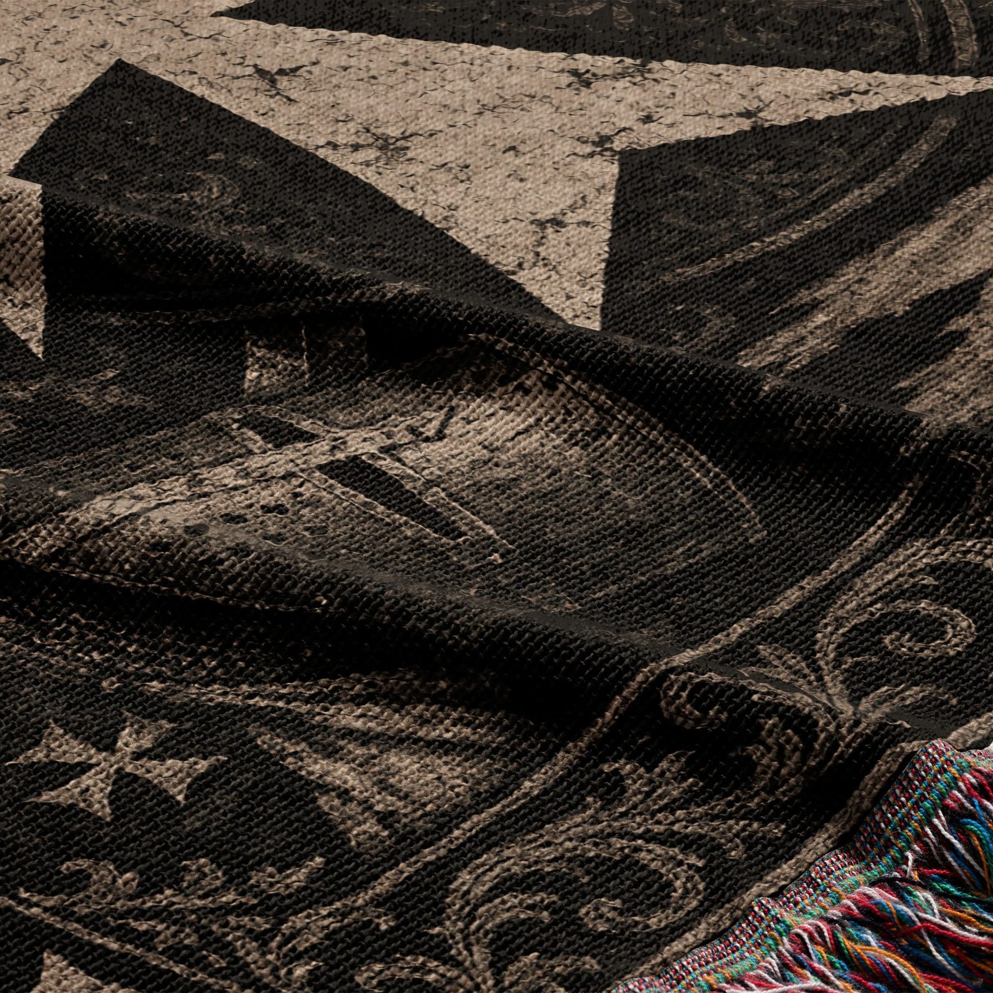 Dark woven throw blanket with an intricate vintage pattern and tasseled edge.