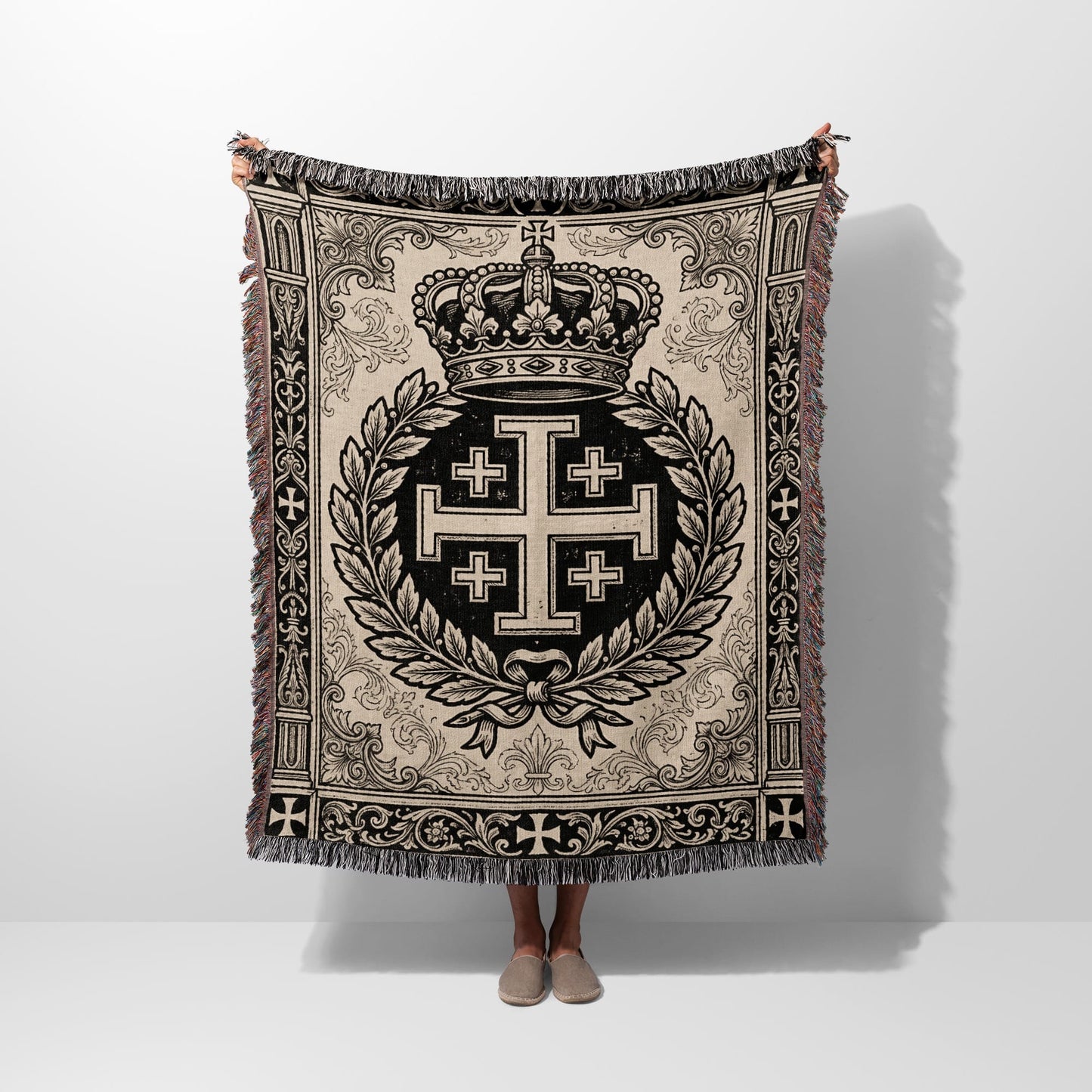 Woven blanket with crown, laurel wreath, and cross emblem on light background.