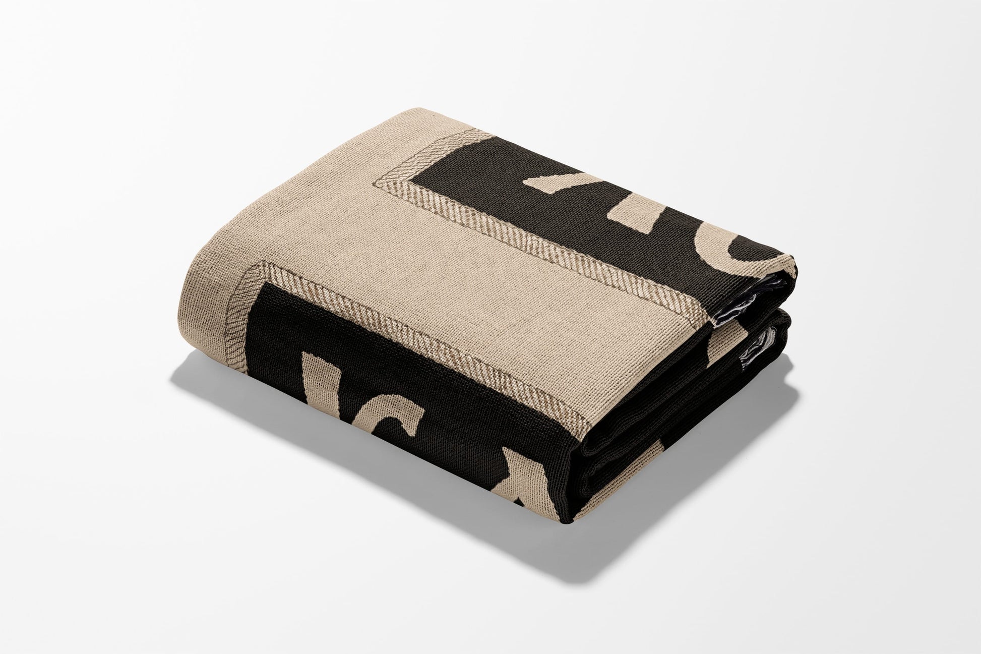 Folded beige blanket with black corner border and logo detail.