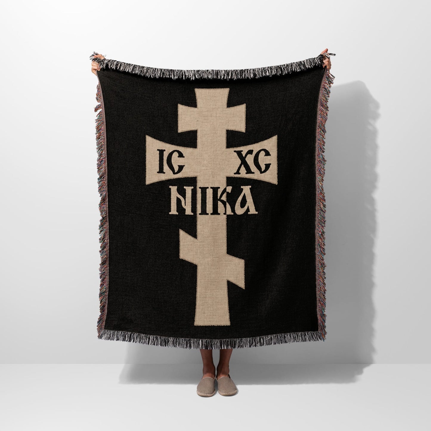 Black blanket with tan cross and inscription, held by a person.