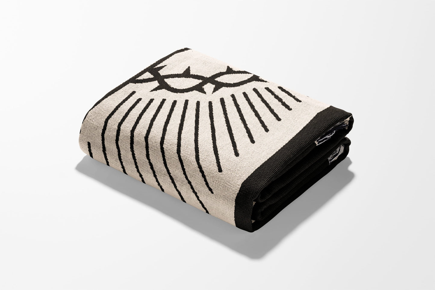 Folded blanket with a black crown of thorns design on a cream background.