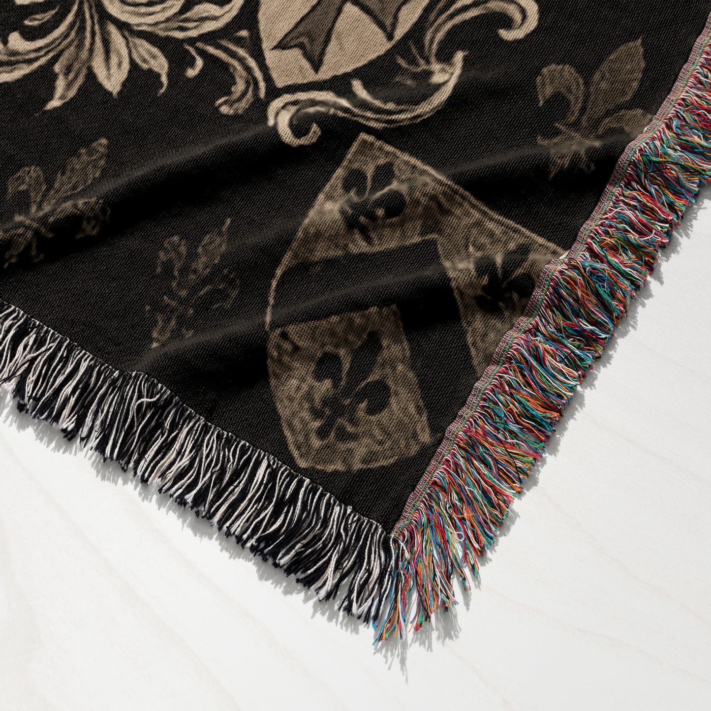 Black tapestry throw with faded crest and fleur-de-lis pattern and fringed edges.