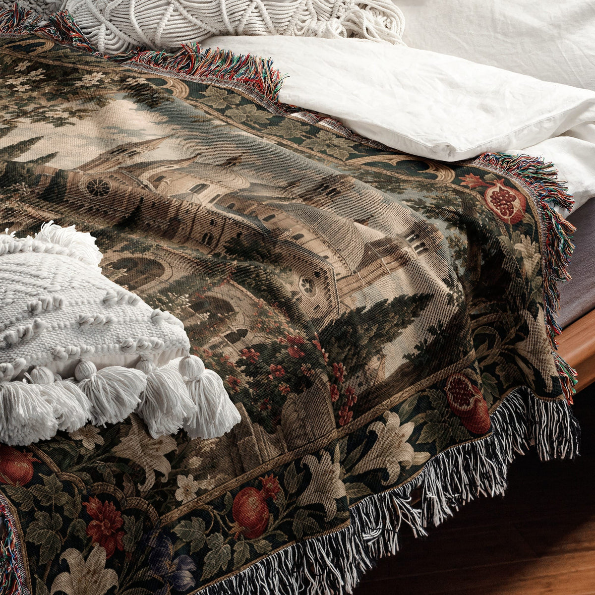 A woven throw blanket with a Renaissance landscape design and tasseled edges draped over a bed.