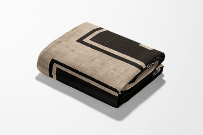 Folded throw blanket with geometric black and beige pattern.