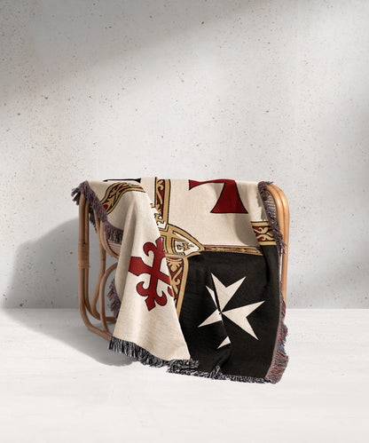 Woven blanket with white, black, red, and gold Maltese cross patterns draped over chair.