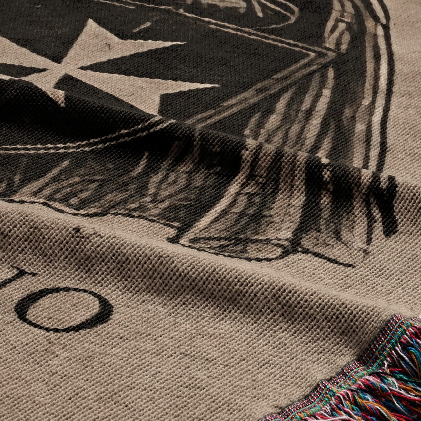 Beige knit throw with a dark graphic design, including a cross and lettering.