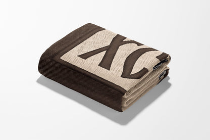 Folded brown blanket with large cream "XC" pattern and dark brown border.