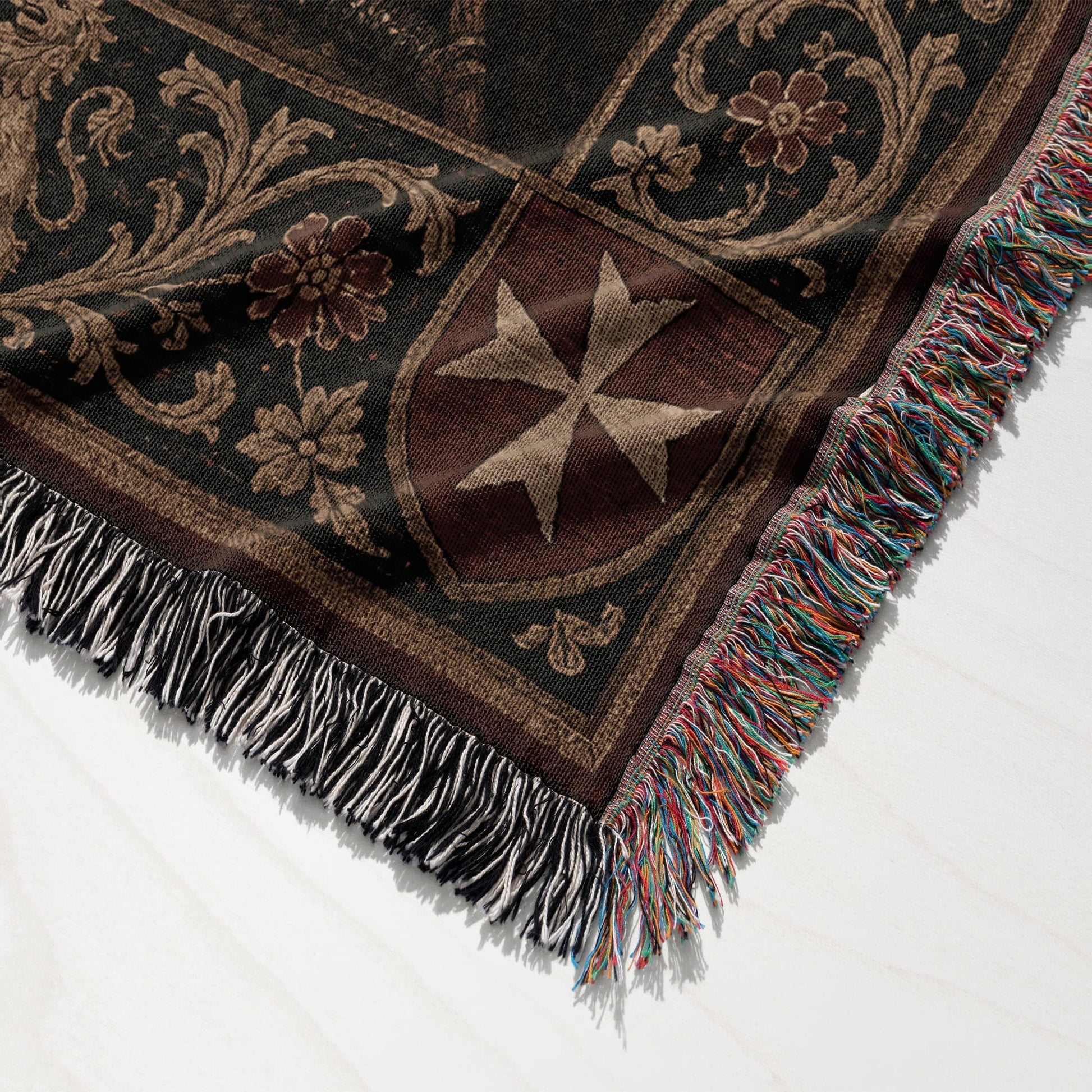 Woven blanket with a brown Maltese cross and floral pattern, fringed edges.