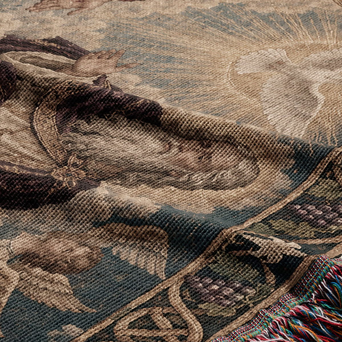 Folded woven tapestry featuring a vintage religious art motif with muted earth tones and fringed edges.
