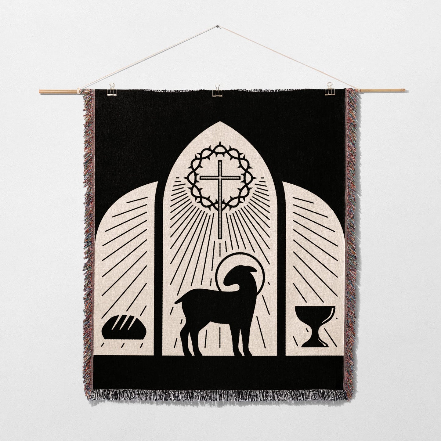 Black tapestry with lamb, cross, bread, and chalice, depicting a religious scene.
