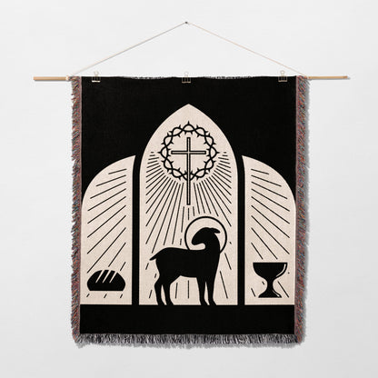 Black tapestry with lamb, cross, bread, and chalice, depicting a religious scene.