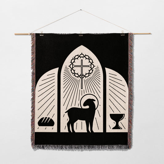 Black tapestry with lamb, cross, bread, and chalice, depicting a religious scene.