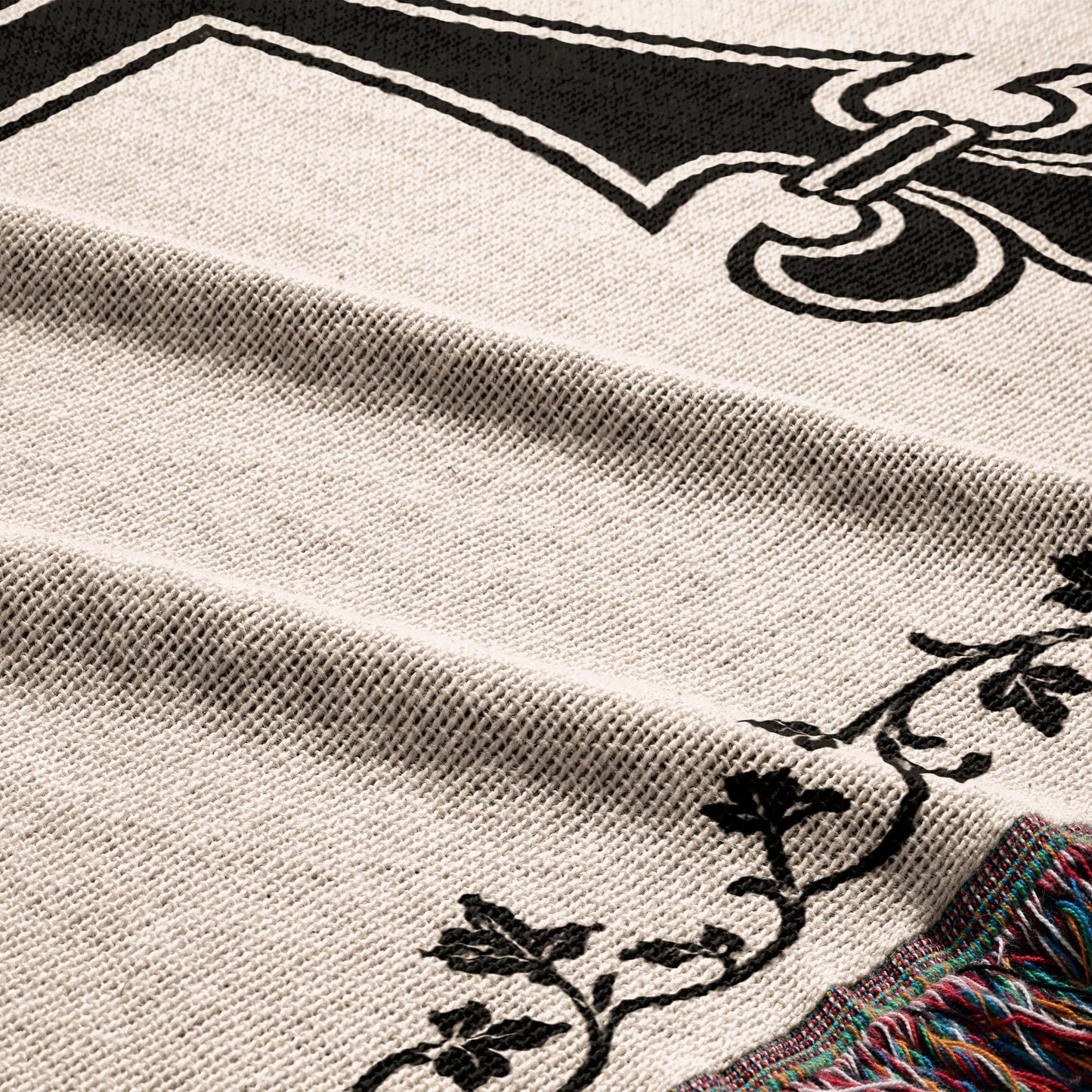 Close-up of cream knit blanket with black ornate design and colorful fringe.