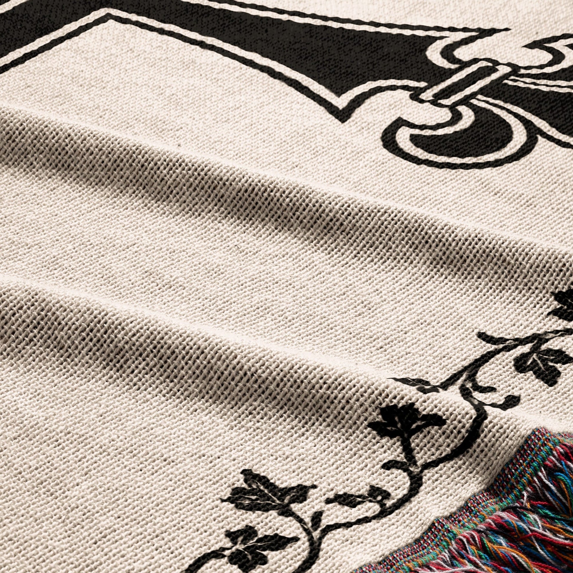 Close-up of cream knit blanket with black ornate design and colorful fringe.