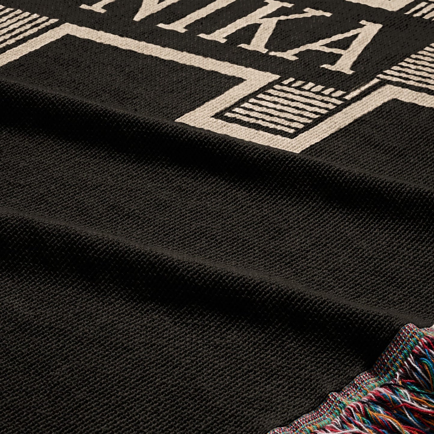 Black woven blanket with white text and colorful fringed edge.