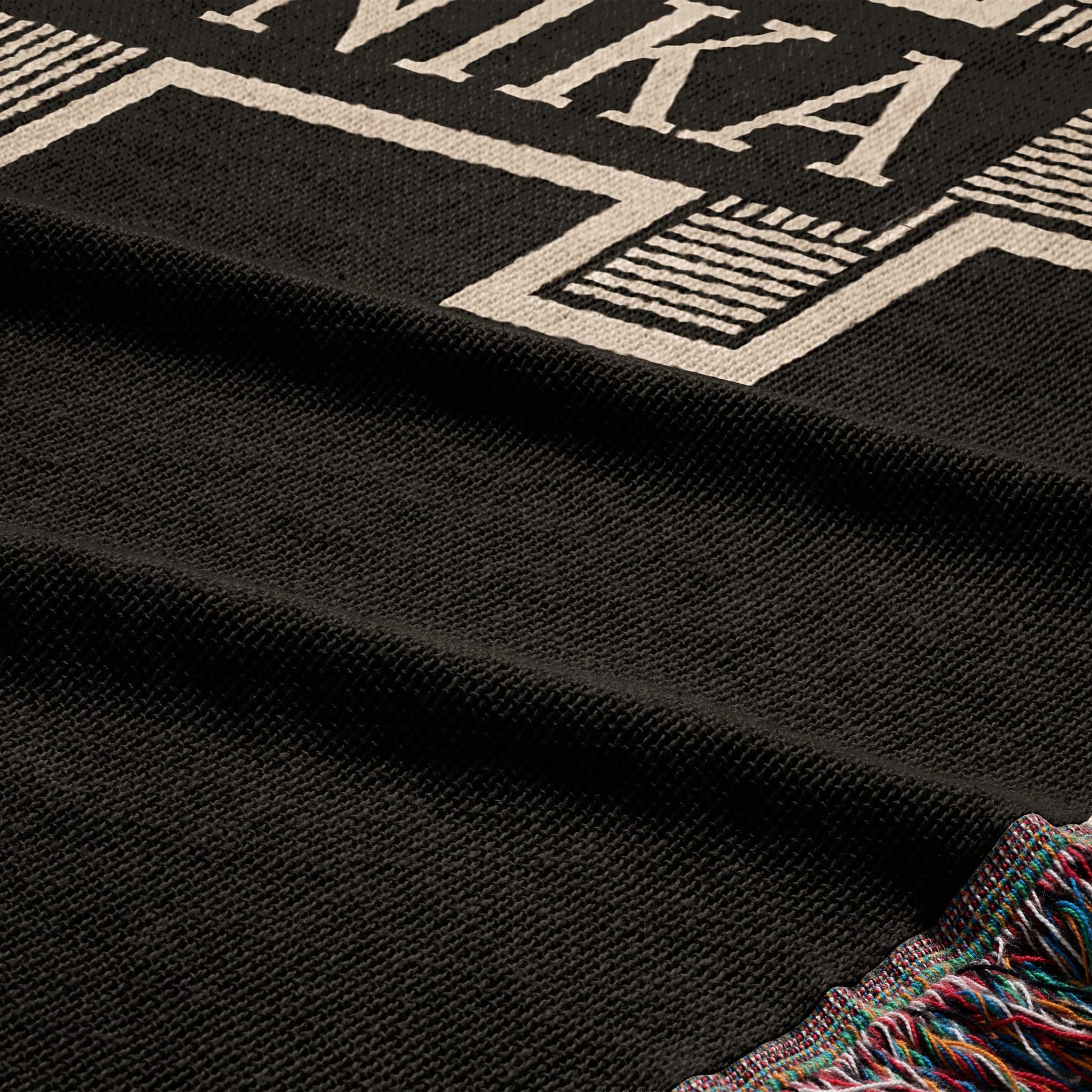 Black woven blanket with white text and colorful fringed edge.