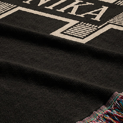Black woven blanket with white text and colorful fringed edge.