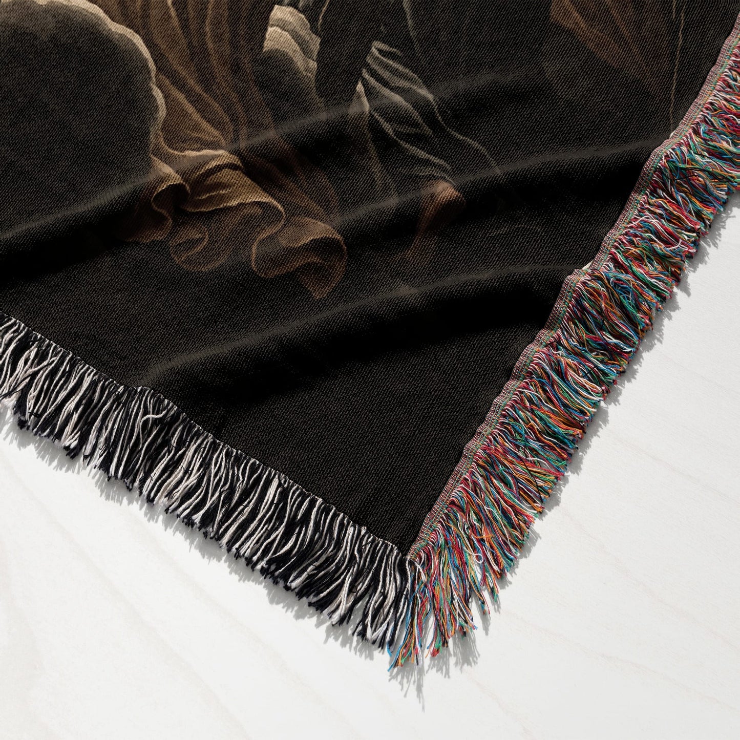 Black woven blanket with fringed edge, featuring a swirling abstract design.