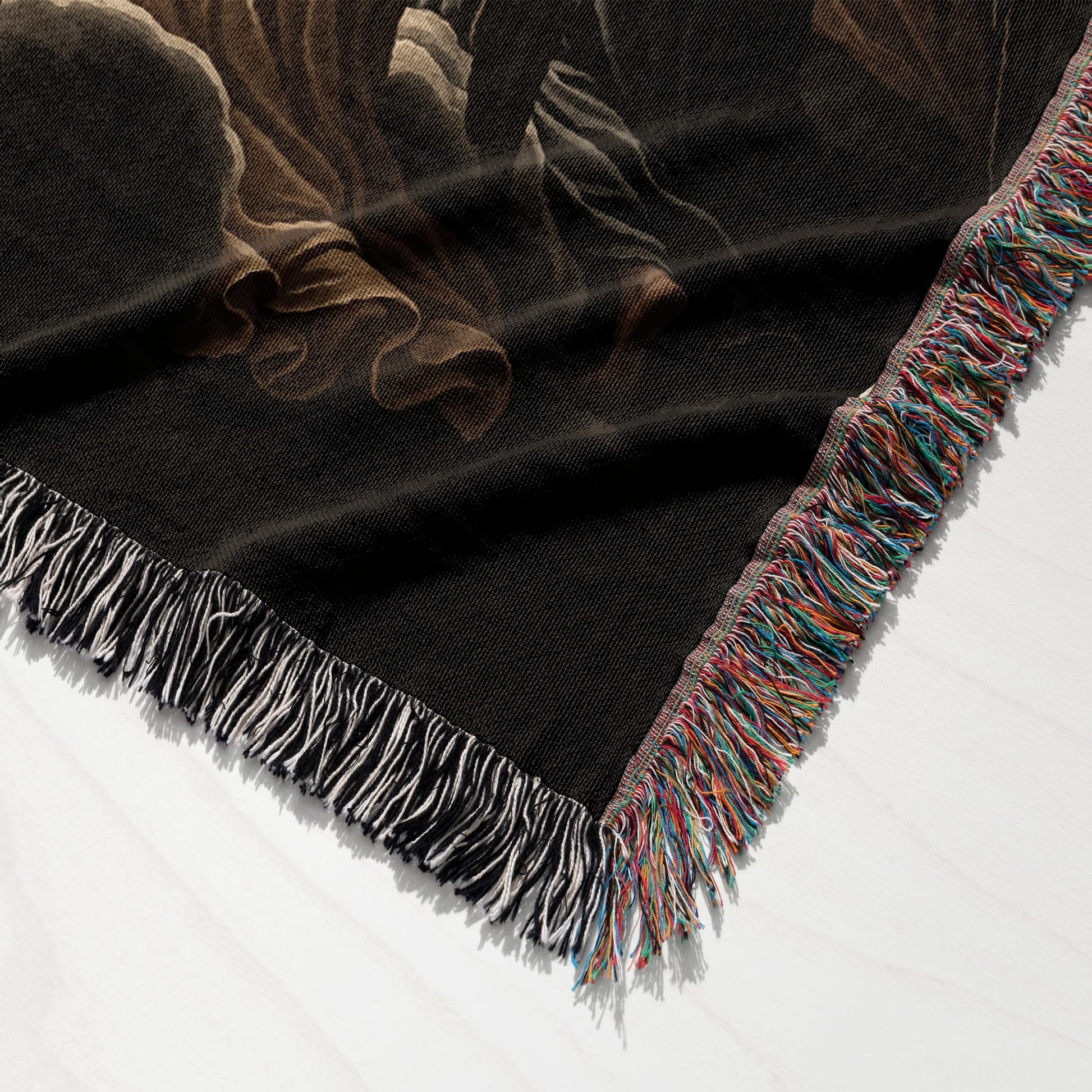Black woven blanket with fringed edge, featuring a swirling abstract design.