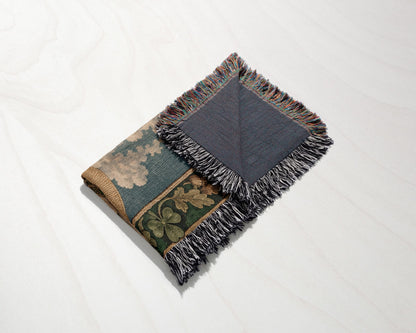A folded woven blanket with a patterned design and fringed edges rests on a light wood surface.