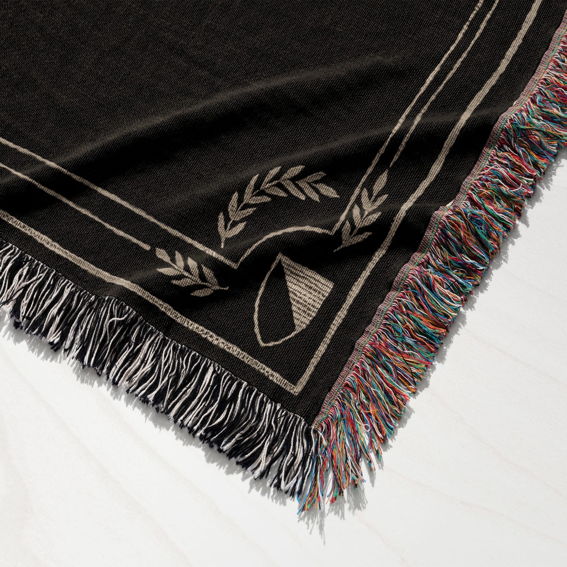 Black woven blanket with beige trim, laurel leaves, shield, and multi-colored fringe.