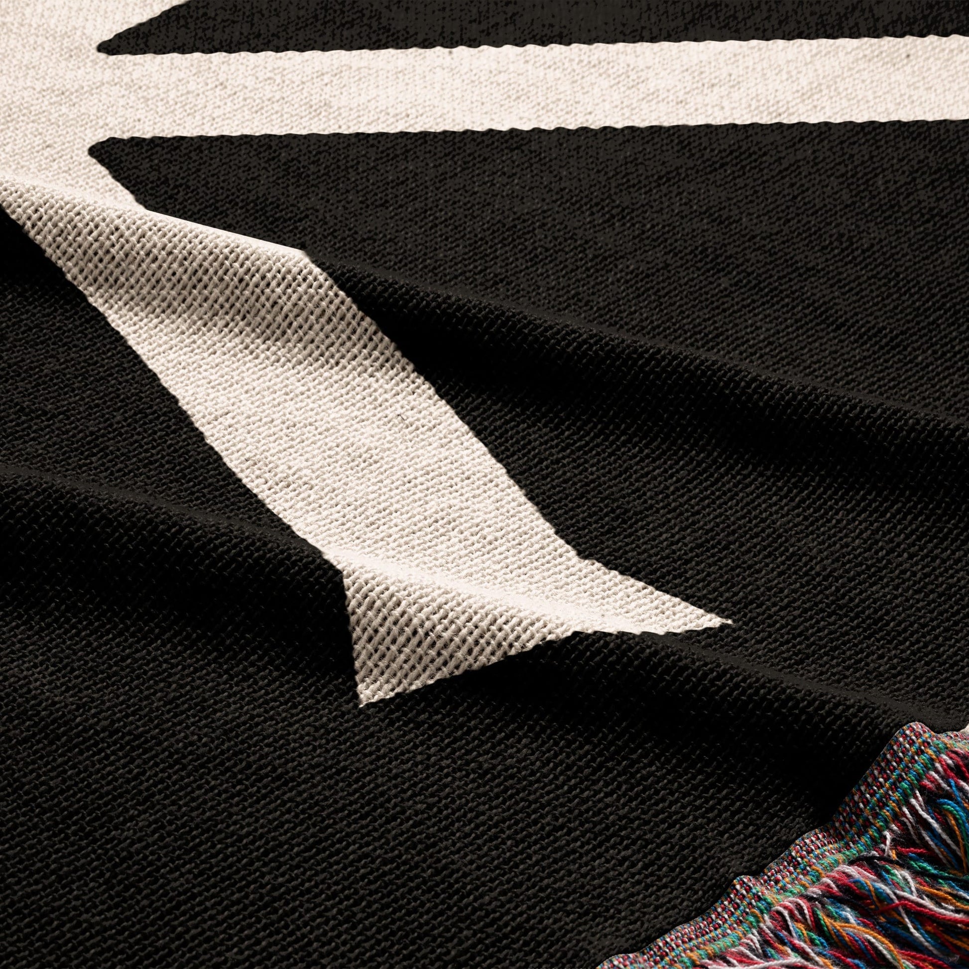 Black throw blanket with cream diagonal stripe and colorful fringe.