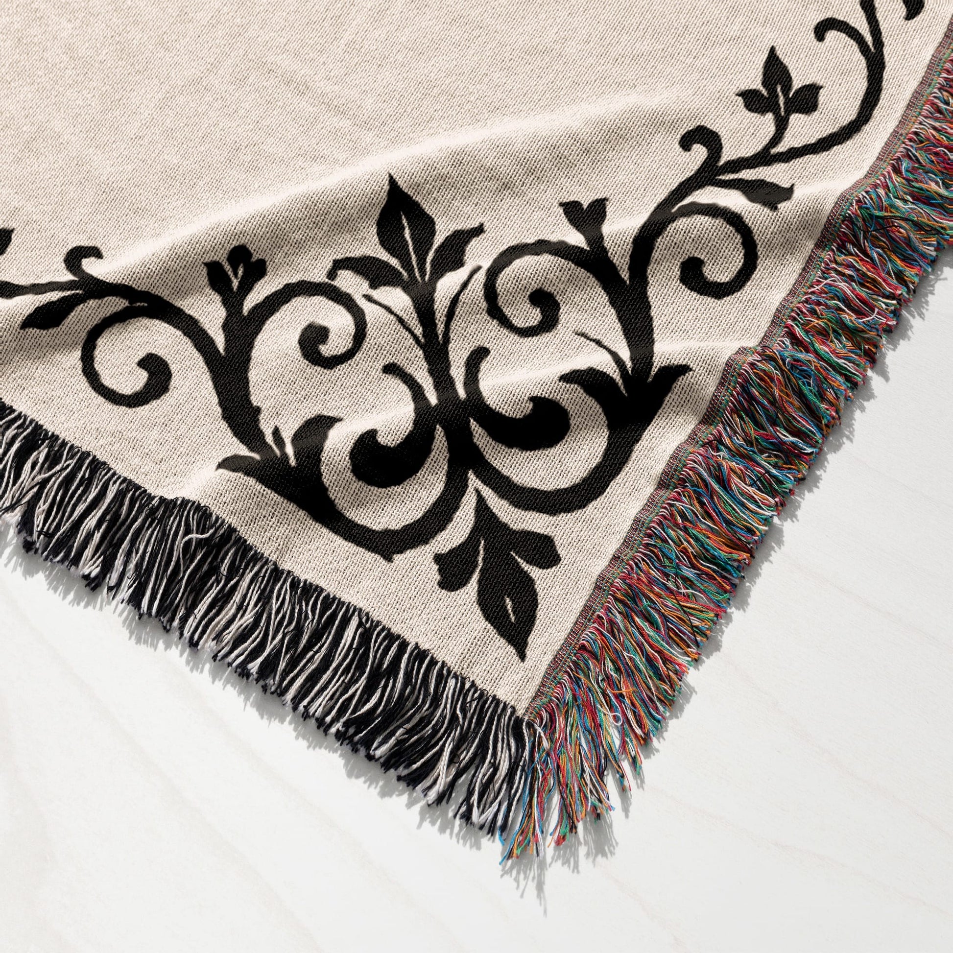 Cream woven throw blanket with black damask pattern and colorful fringe.