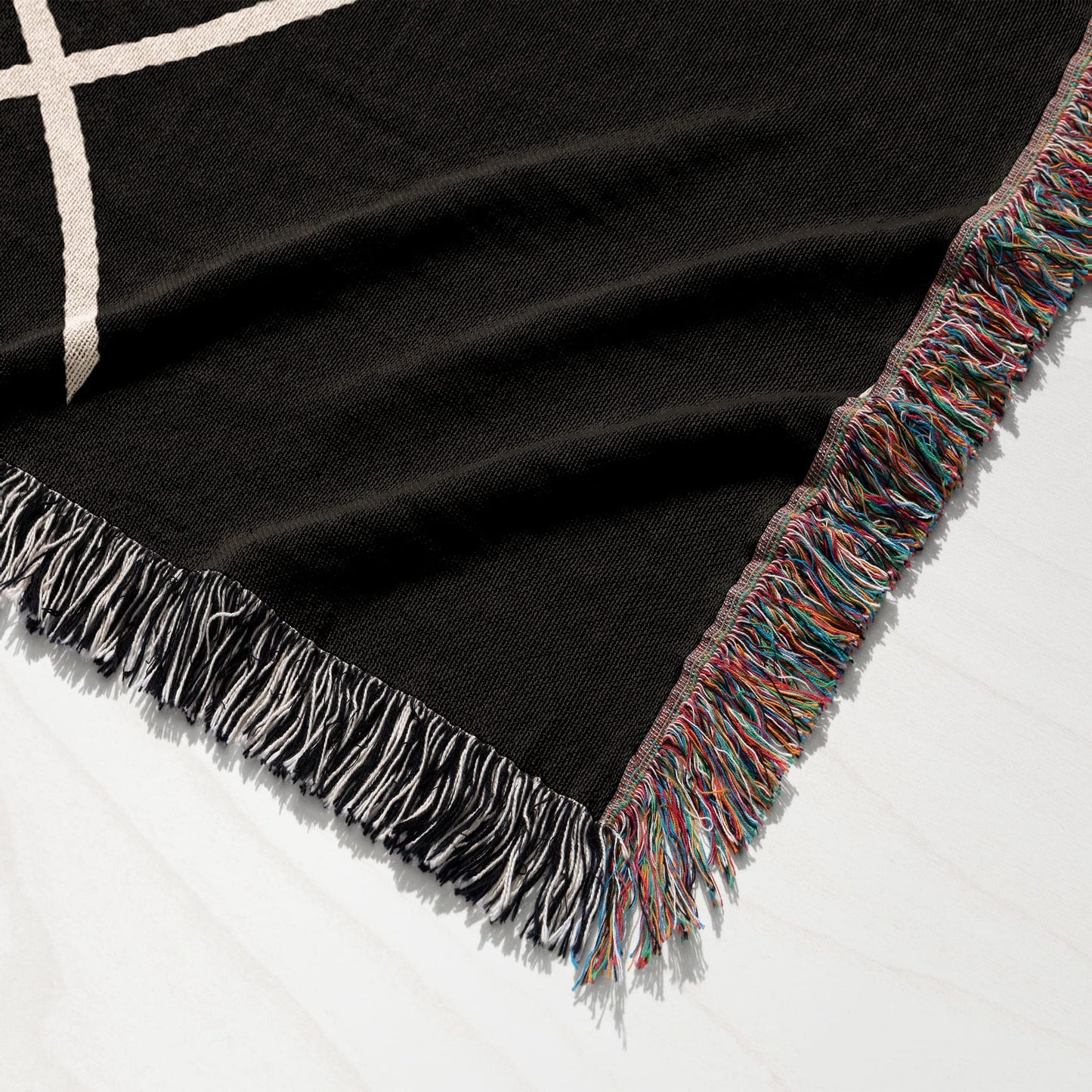 Black woven throw blanket with colorful fringe and white geometric pattern.