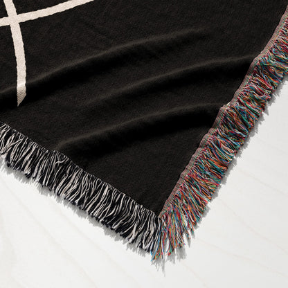 Black woven throw blanket with colorful fringe and white geometric pattern.