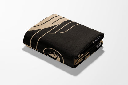 Black blanket with tan geometric pattern, folded on a white background.