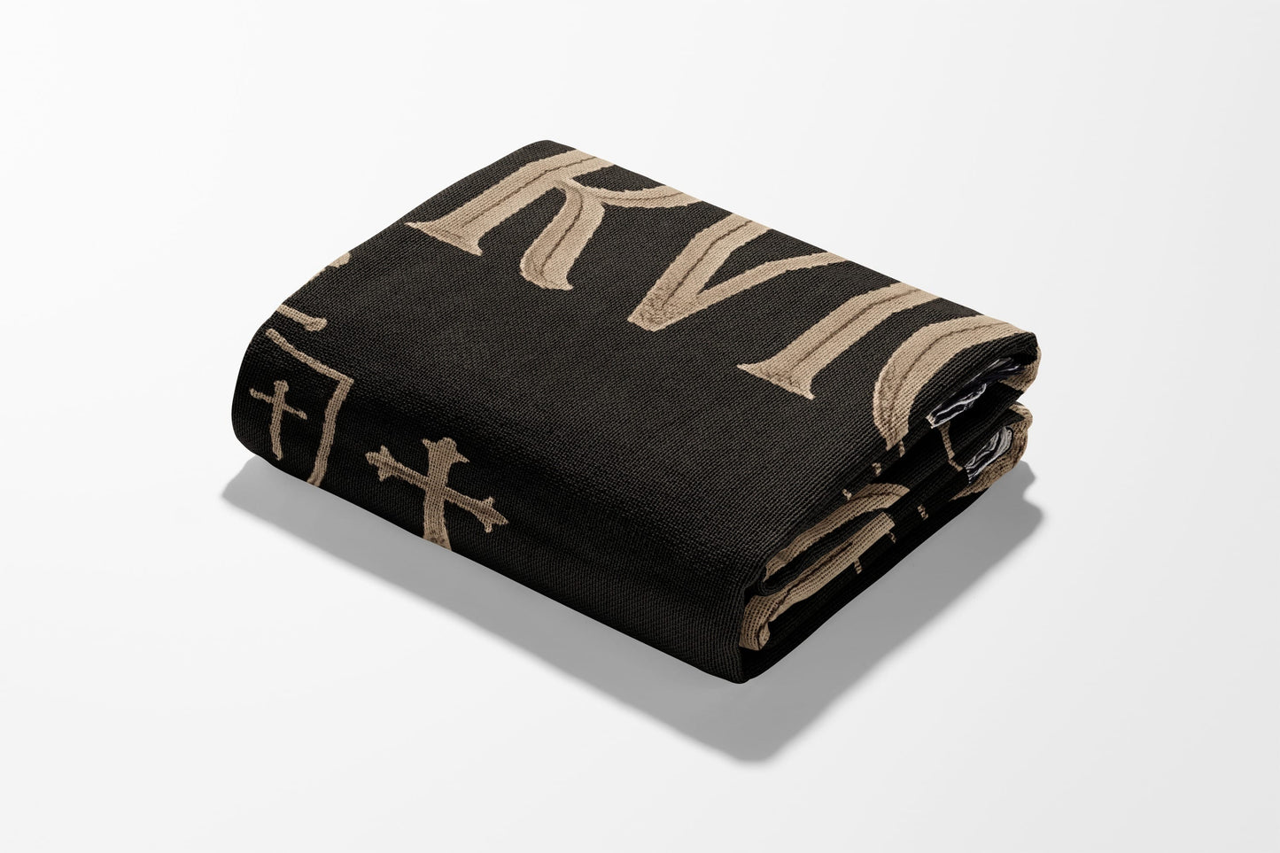 Black folded blanket with embroidered tan capital letters and crosses.