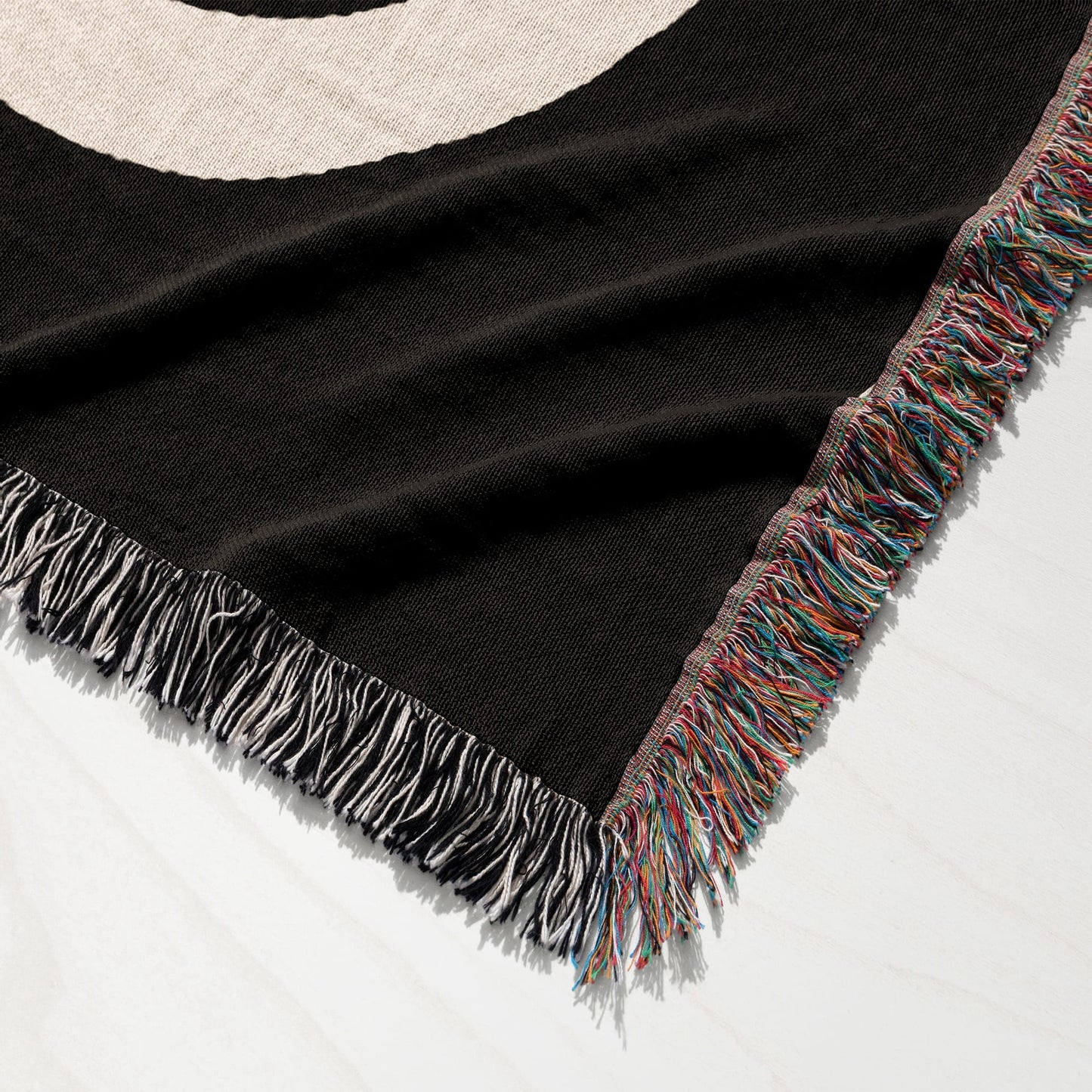 Black woven blanket with colorful fringe and a partial white circle design.