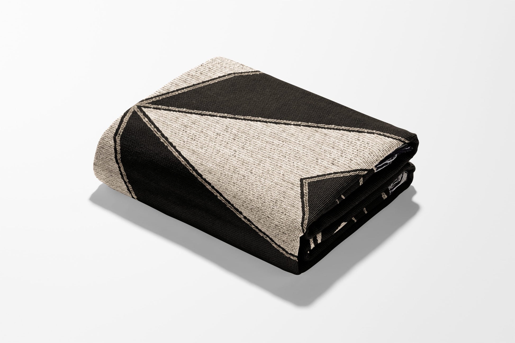 Folded blanket with geometric black and tan pattern against white background.