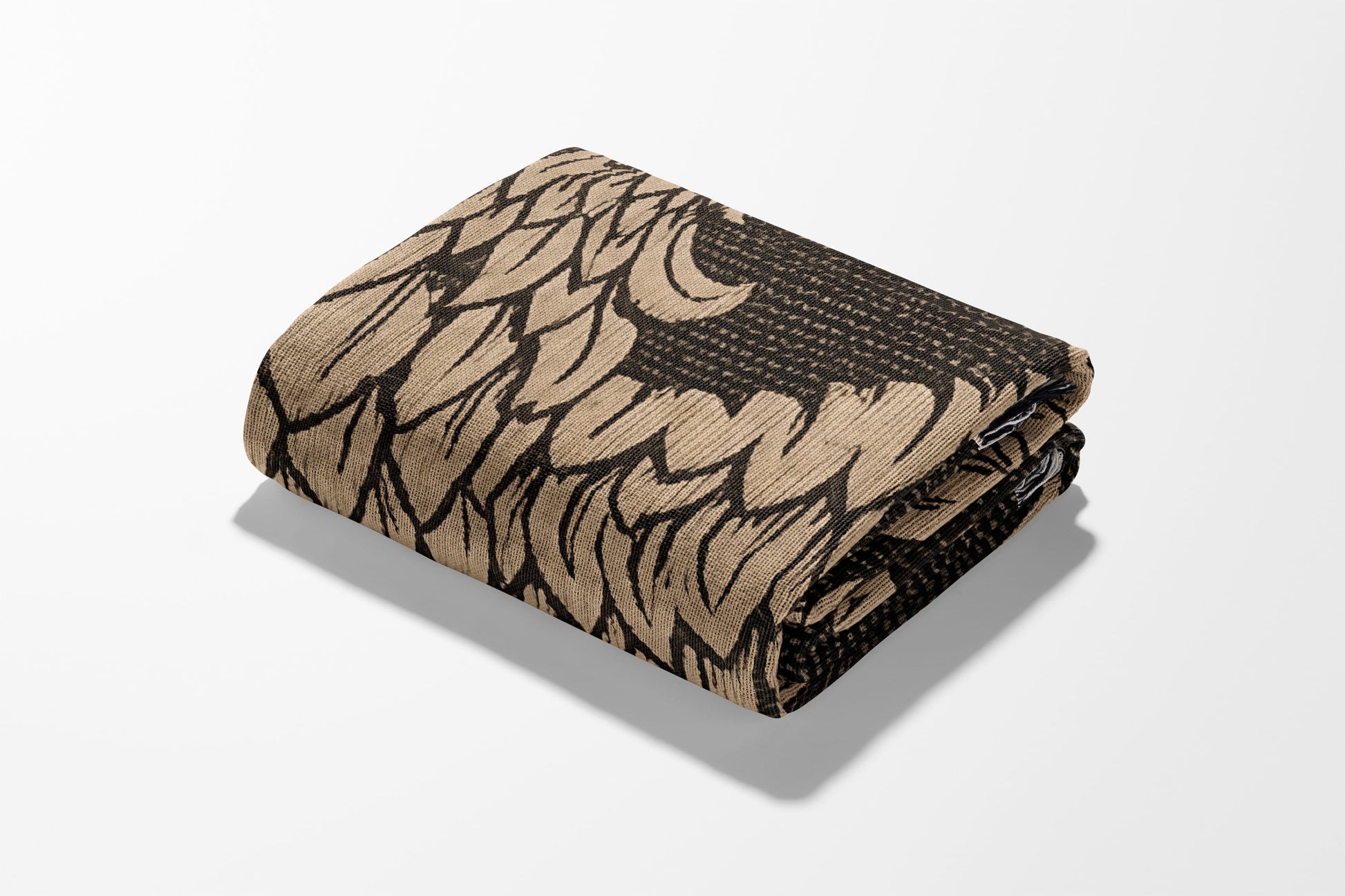 Folded throw blanket with a repeating abstract feather pattern in black and tan.