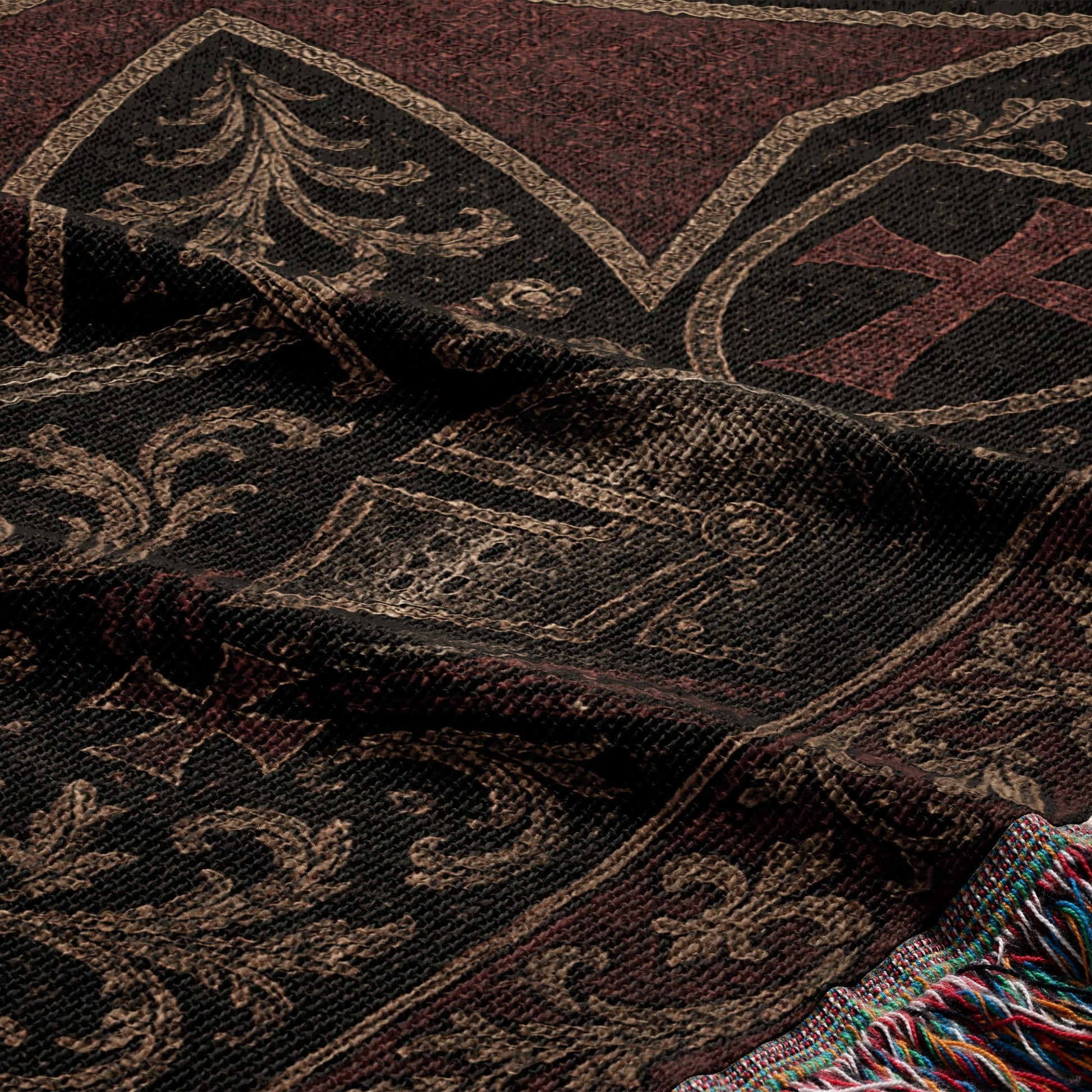 Dark woven blanket with intricate scrollwork and a red cross emblem, fringed edge.