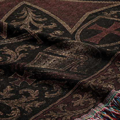 Dark woven blanket with intricate scrollwork and a red cross emblem, fringed edge.