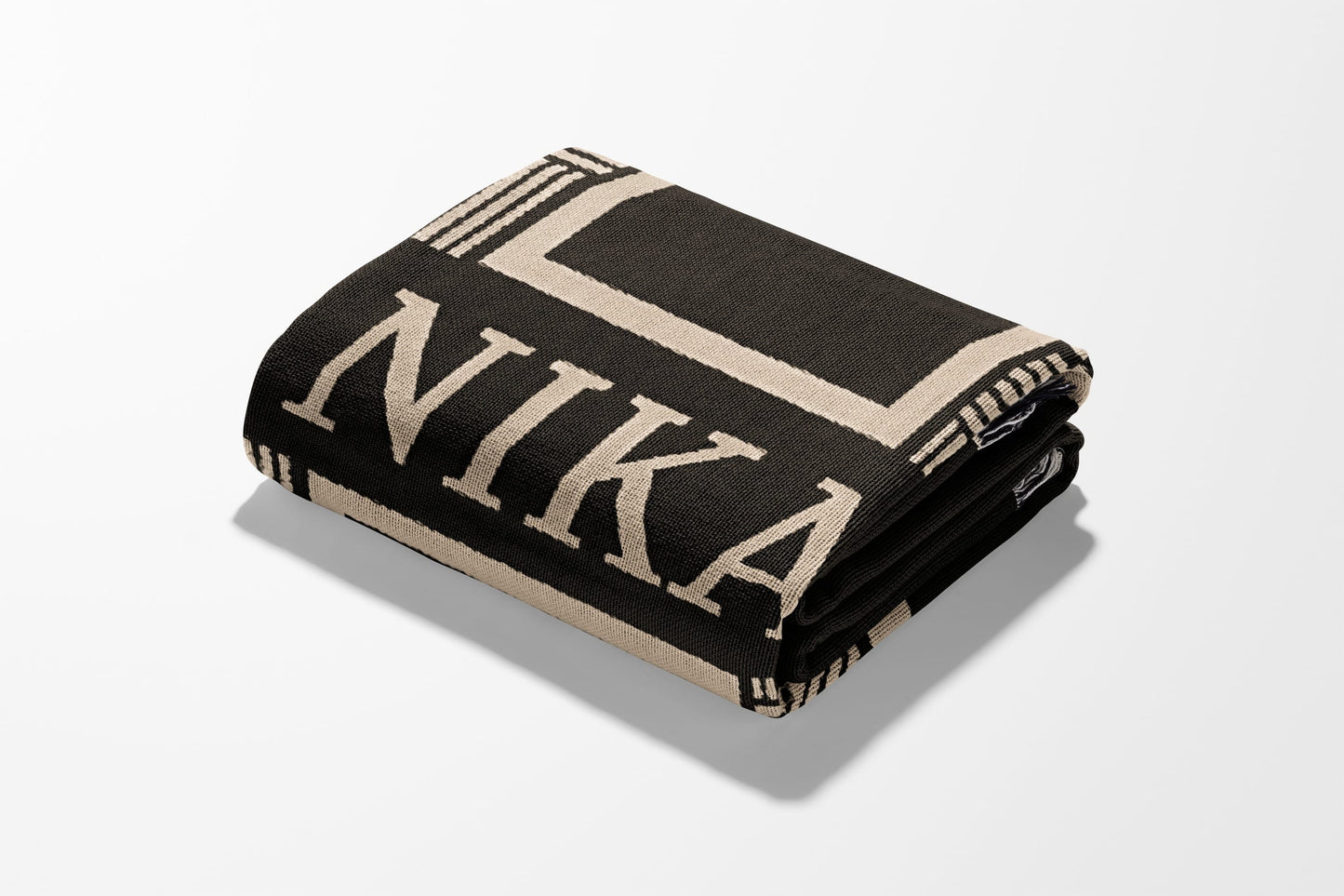 Folded black throw blanket with beige "NIKA" text and geometric border.