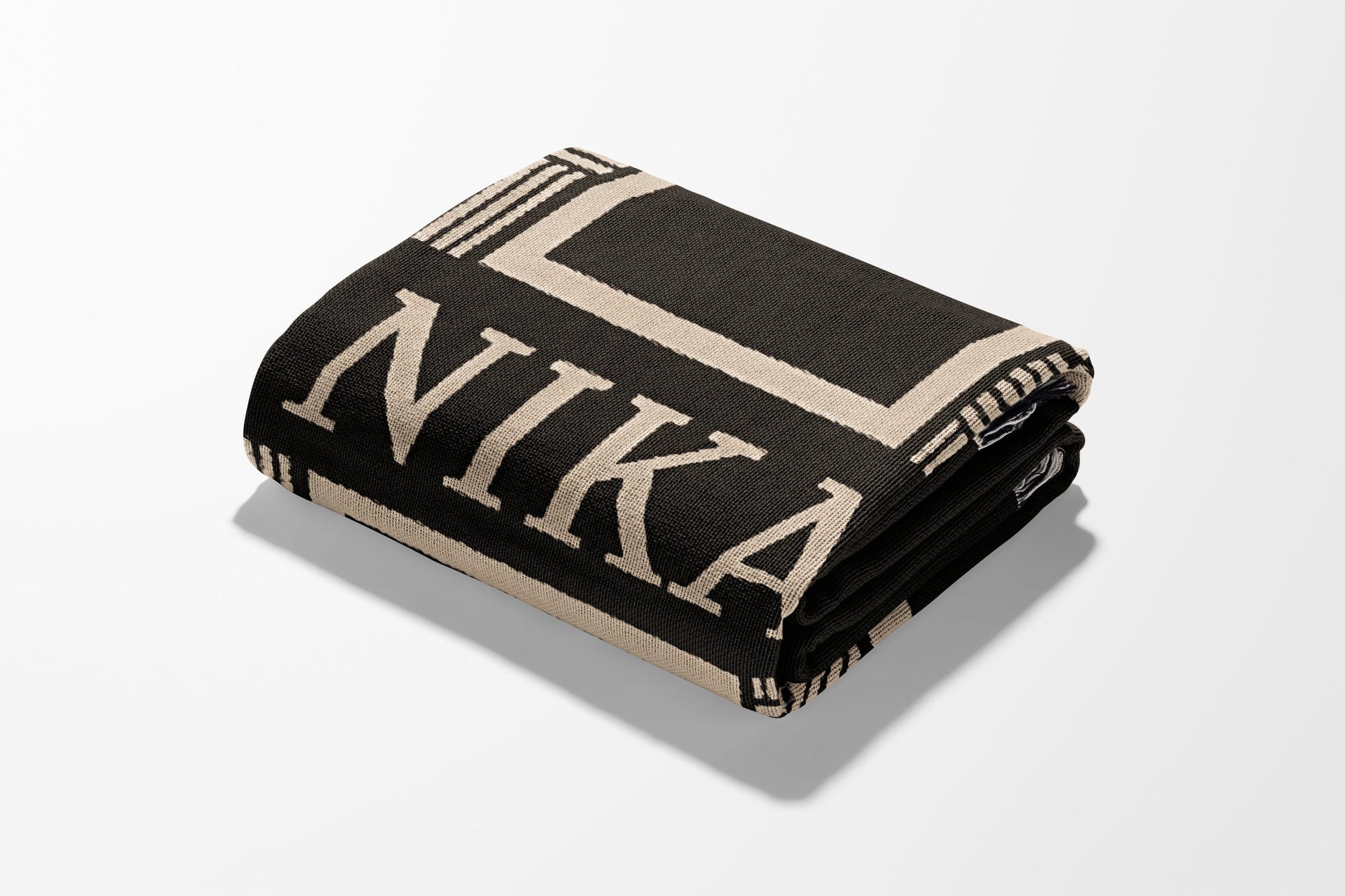 Folded black throw blanket with beige "NIKA" text and geometric border.