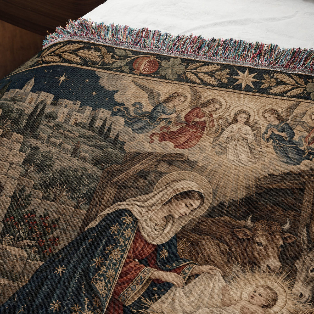 Woven tapestry blanket depicting the Nativity scene with Mary, baby Jesus, animals, angels, and a walled city.