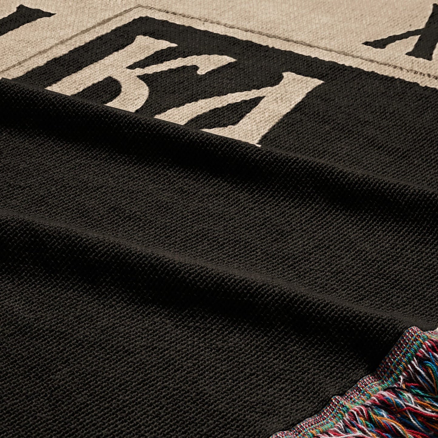 Black woven blanket with multicolor fringe and large white text.