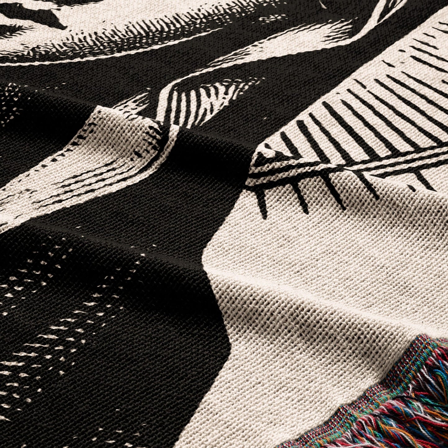Close-up of a black and white knit blanket with colorful fringe detail.