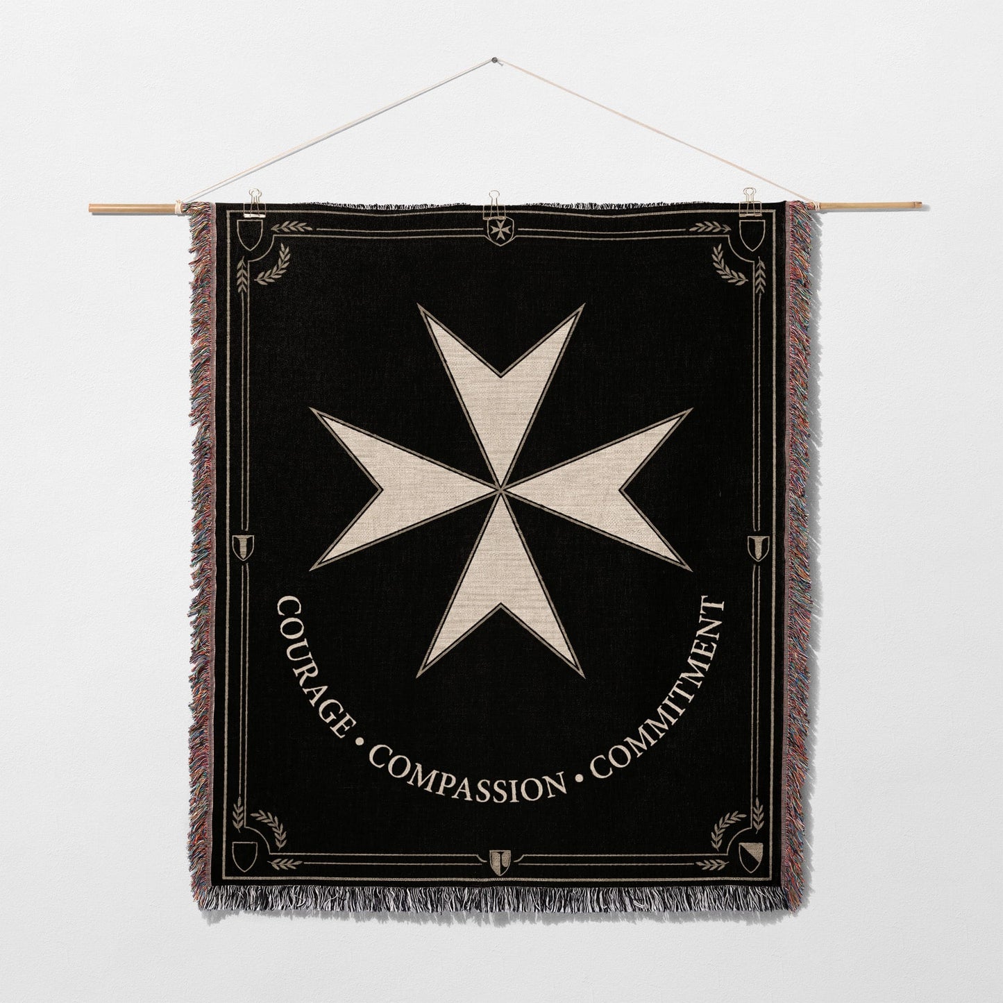 Black tapestry featuring a white Maltese cross and the words "COURAGE • COMPASSION • COMMITMENT".
