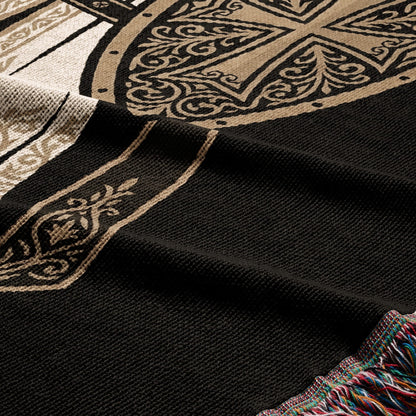 Black woven throw blanket with intricate tan scrolling patterns and a fringed edge.