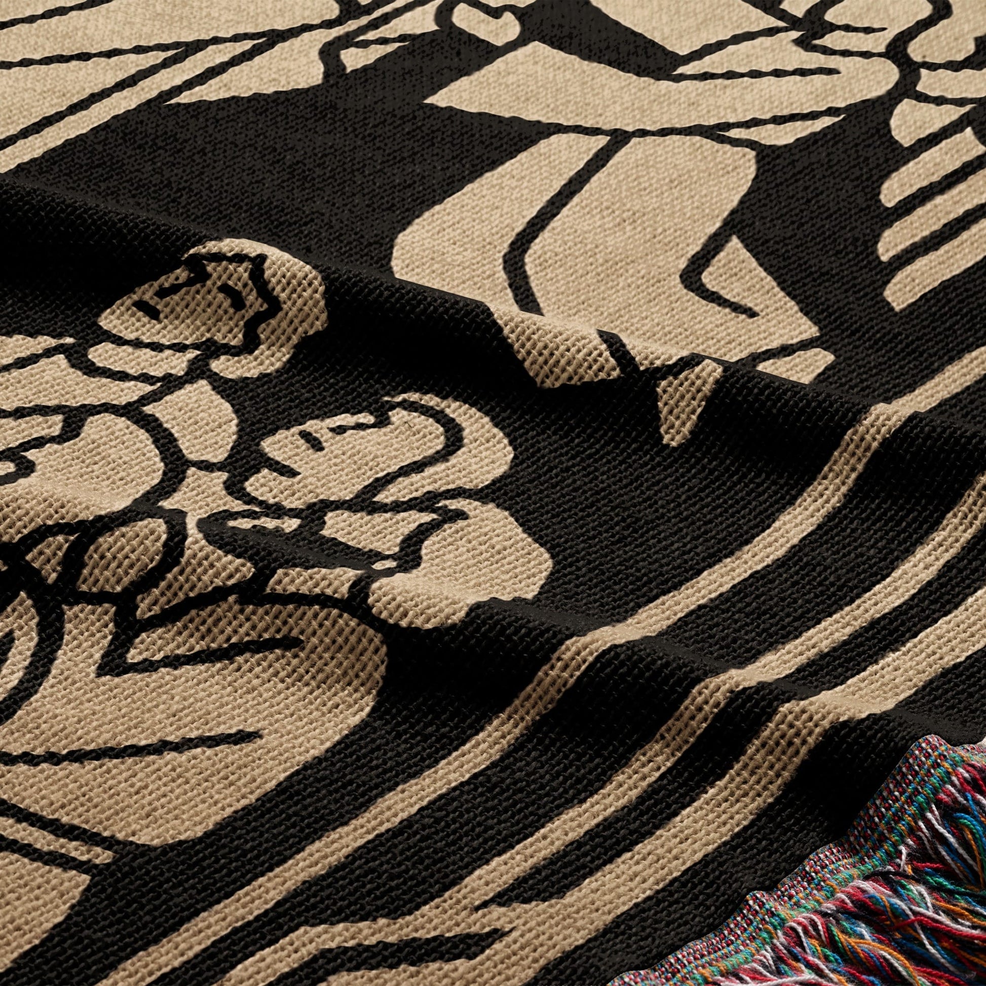 Black and tan woven blanket with floral design and fringed edge.