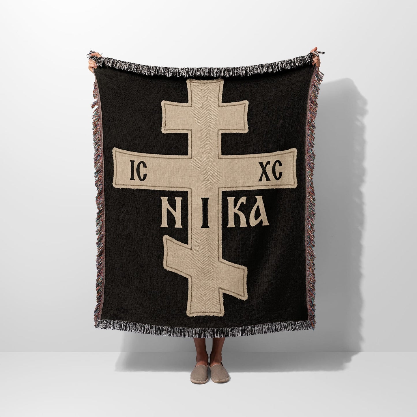 Fringe-trimmed black throw blanket with a prominent beige Orthodox Christian cross and "IC XC NIKA" inscription.