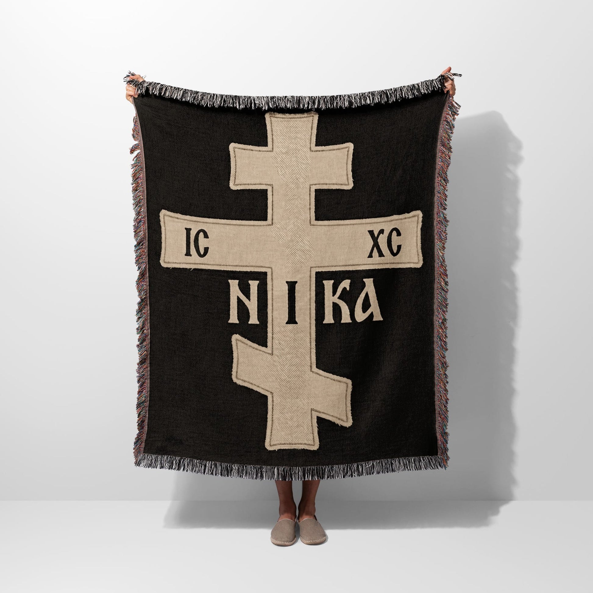 Fringe-trimmed black throw blanket with a prominent beige Orthodox Christian cross and "IC XC NIKA" inscription.
