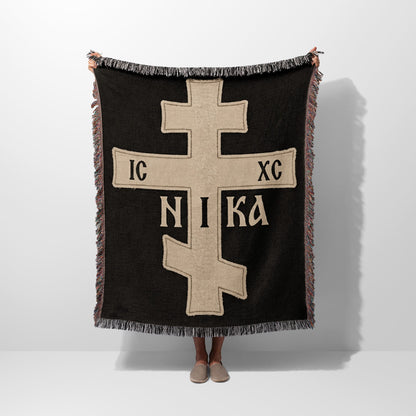 Fringe-trimmed black throw blanket with a prominent beige Orthodox Christian cross and "IC XC NIKA" inscription.