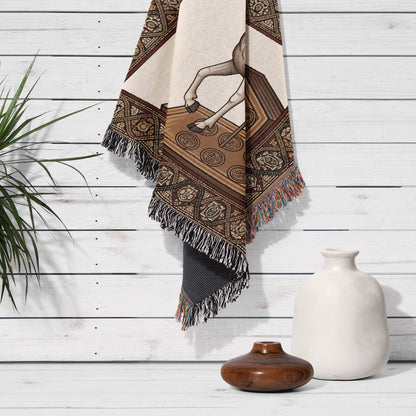 Beige and brown patterned throw blanket with fringed edges hangs on white wood wall.